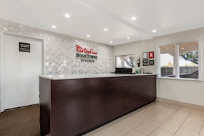 A reception desk with a geometric wall design, a 'Manager on Duty' sign, and a window with a view of trees and a fence. - Red Roof Inn Georgetown, KY (Georgetown)