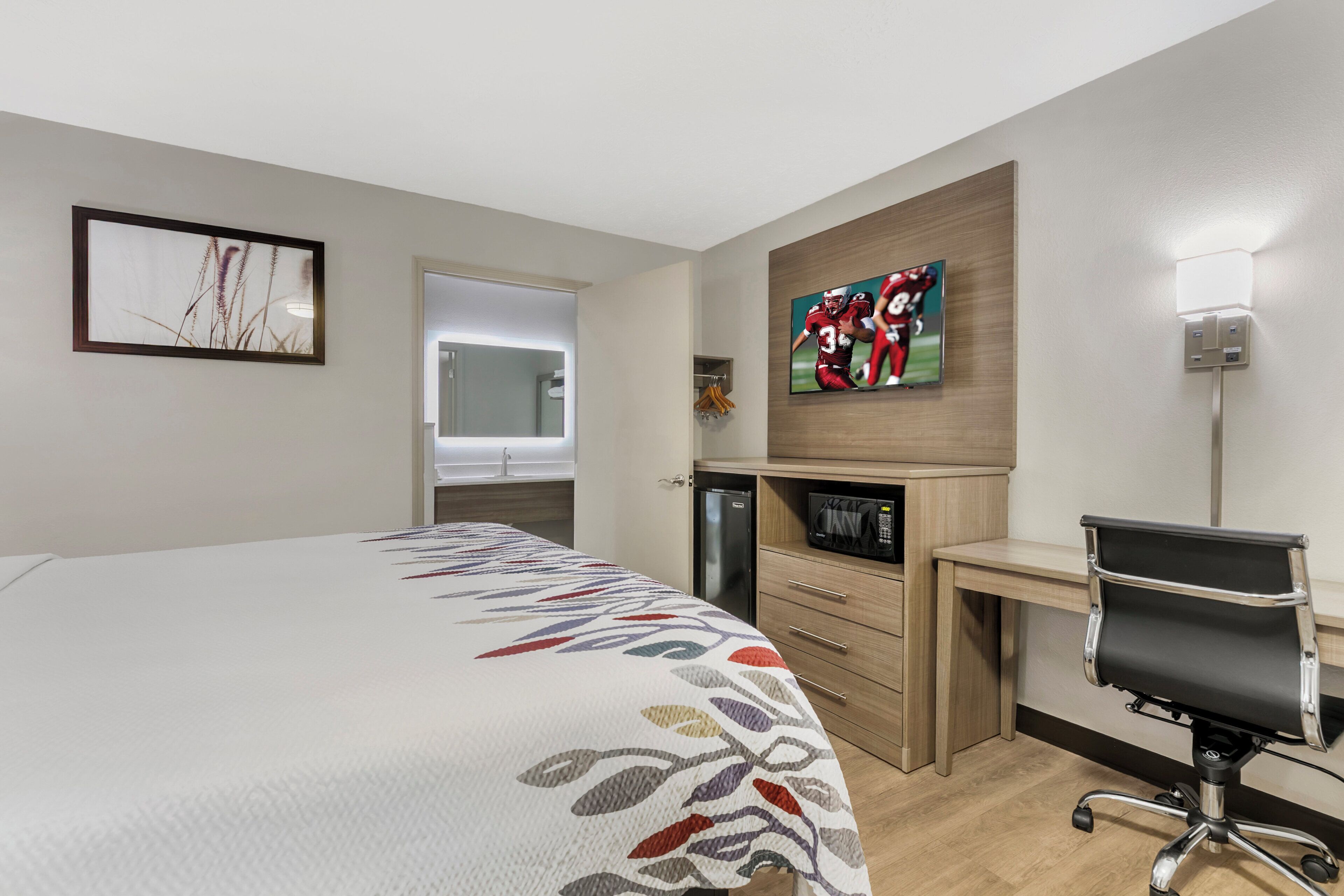 Habitación de hotel con cama, escritorio, silla, microondas y televisor.