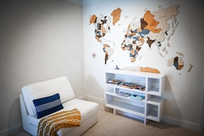 A room with a white sofa, a world map on the wall, and a white bookshelf with books.
