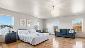 Um quarto espaçoso com uma cama grande, um sofá azul escuro e várias janelas com vista para o exterior.