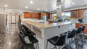 Uma cozinha moderna com uma ilha grande, banquetas, eletrodomésticos de aço inoxidável e armários de madeira.