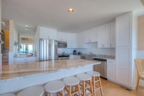Una cocina moderna con armarios blancos, electrodomésticos de acero inoxidable y una isla de mármol con taburetes.