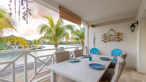 A dining area with a white table set for four, wicker chairs, and a view of the ocean. - Beautiful condo with sea view (Kralendijk)