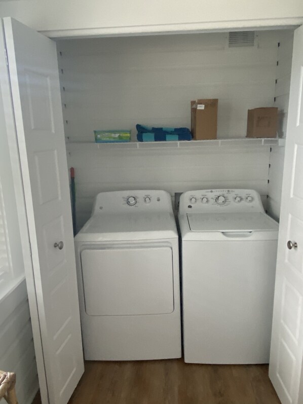 A laundry room with two white dryers and a shelf above them.