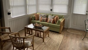 A cozy living room with a green sofa, wicker chairs, a coffee table, and white shutters on the windows. - Coquina Cottage on Vilano Beach (St. Augustine)