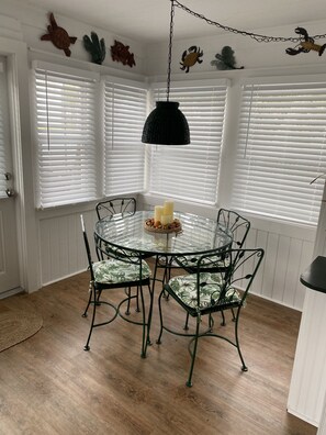 Een eethoek met een ronde tafel en stoelen, witte raamluiken en decoratieve wanddecoratie.