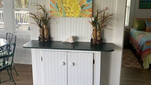 A kitchen island with a white cabinet and a painting of yellow flowers and green leaves above it. - Coquina Cottage on Vilano Beach (St. Augustine)