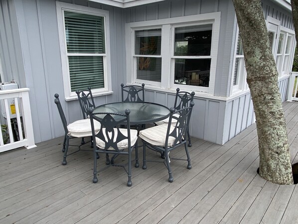 A deck with a round table and six chairs, surrounded by windows with white trim.