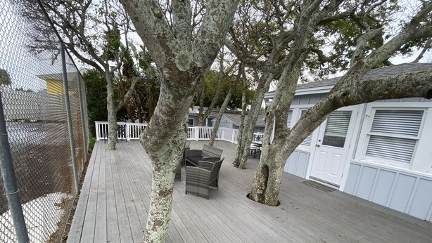 A wooden deck with a white fence, a covered seating area, and a white building with shutters. - Coquina Cottage on Vilano Beach (St. Augustine)