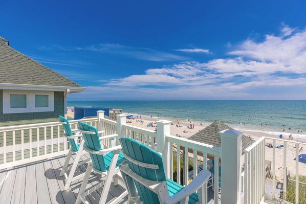 A wooden deck with chairs overlooking a beach.