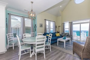 A spacious living area with a round dining table, white chairs, a blue sofa, and a wicker chair. - Sea-Renity Now! Stress Free Vacation in the Heart of Surf City (Surf City)