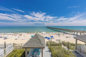 A beach with a pier extending into the water, beach umbrellas, and a gazebo. - Sea-Renity Now! Stress Free Vacation in the Heart of Surf City (Surf City)