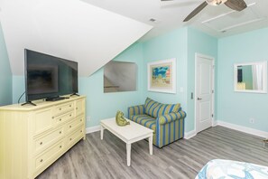 A room with a television on a stand, a sofa, a small table with a frog decoration, and a ceiling fan.