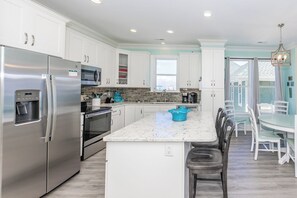 A modern kitchen with stainless steel appliances, a marble countertop, and a dining area with white chairs.