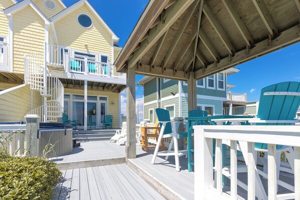 A wooden deck with outdoor seating and a covered area, overlooking a beach.