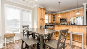 A modern kitchen with wooden cabinets, a central island, and a dining area with a table and chairs. - Pier Pressure - Amazing Oceanfront 6 BR Half Duplex; Hot Tub and more! Pet (Surf City)