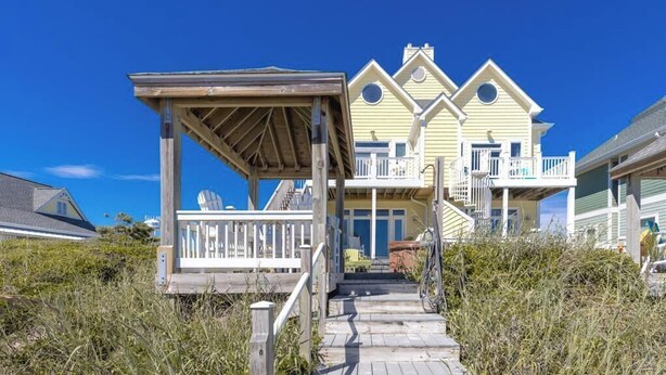 Ein Strandhaus mit überdachter Veranda, einem Balkon und einem Weg zum Eingang.