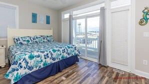 Ein Schlafzimmer mit Bett, Deckenventilator und Blick auf eine Stadtlandschaft durch große Fenster.
