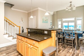 A kitchen with granite countertops, wooden cabinets, a stainless steel sink, and a dining area with a view of the ocean.