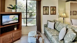 Uma sala de estar com televisão, sofá, mesa e janela com persianas.