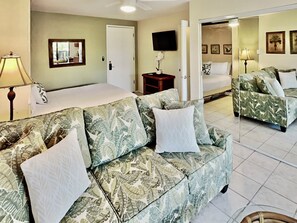 A hotel room with a bed, a sofa, a television, and a mirror.