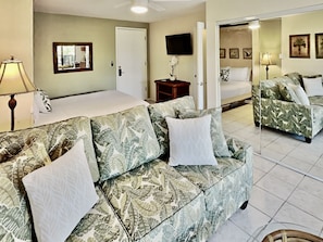 A hotel room with a bed, a sofa, a TV, and a door.