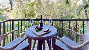 Uma mesa redonda com cadeiras de vime, uma garrafa de vinho e um copo em uma varanda com vista para vegetação exuberante e árvores.