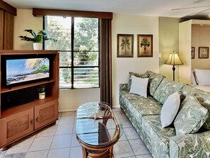 A living room with a television, a sofa, a table, and a window with blinds.