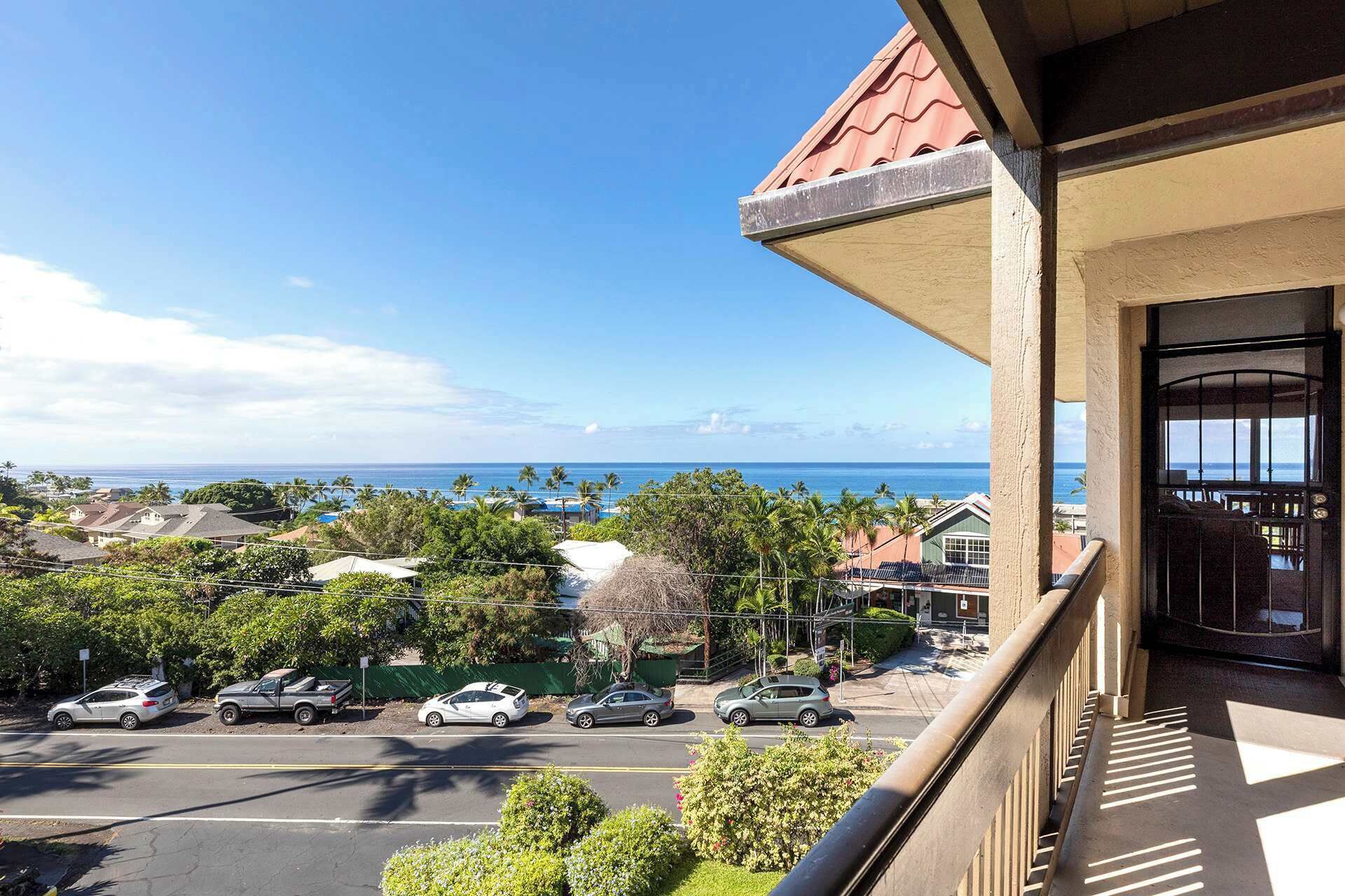 A balcony with a view of the ocean and a street with parked cars.
