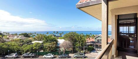 A balcony with a view of the ocean and a street with parked cars.
