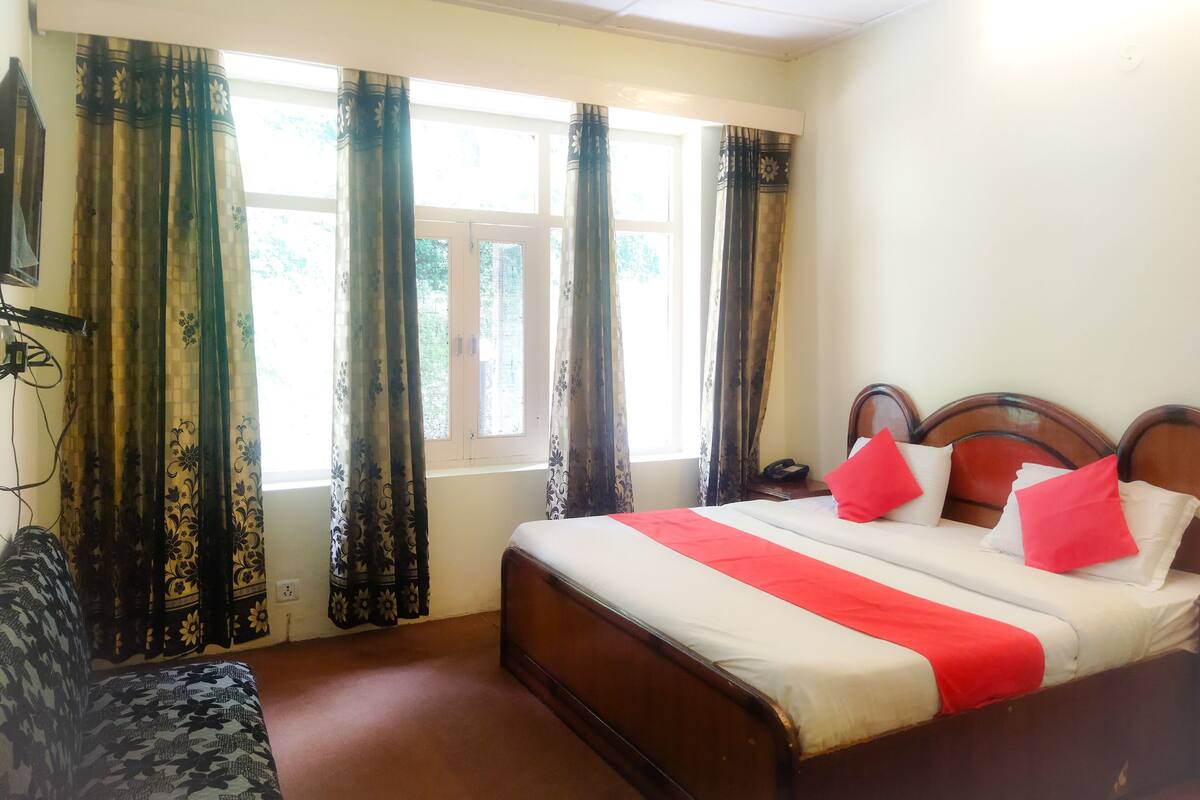 A hotel room with a bed, a sofa, a window with curtains, and a ceiling light.
