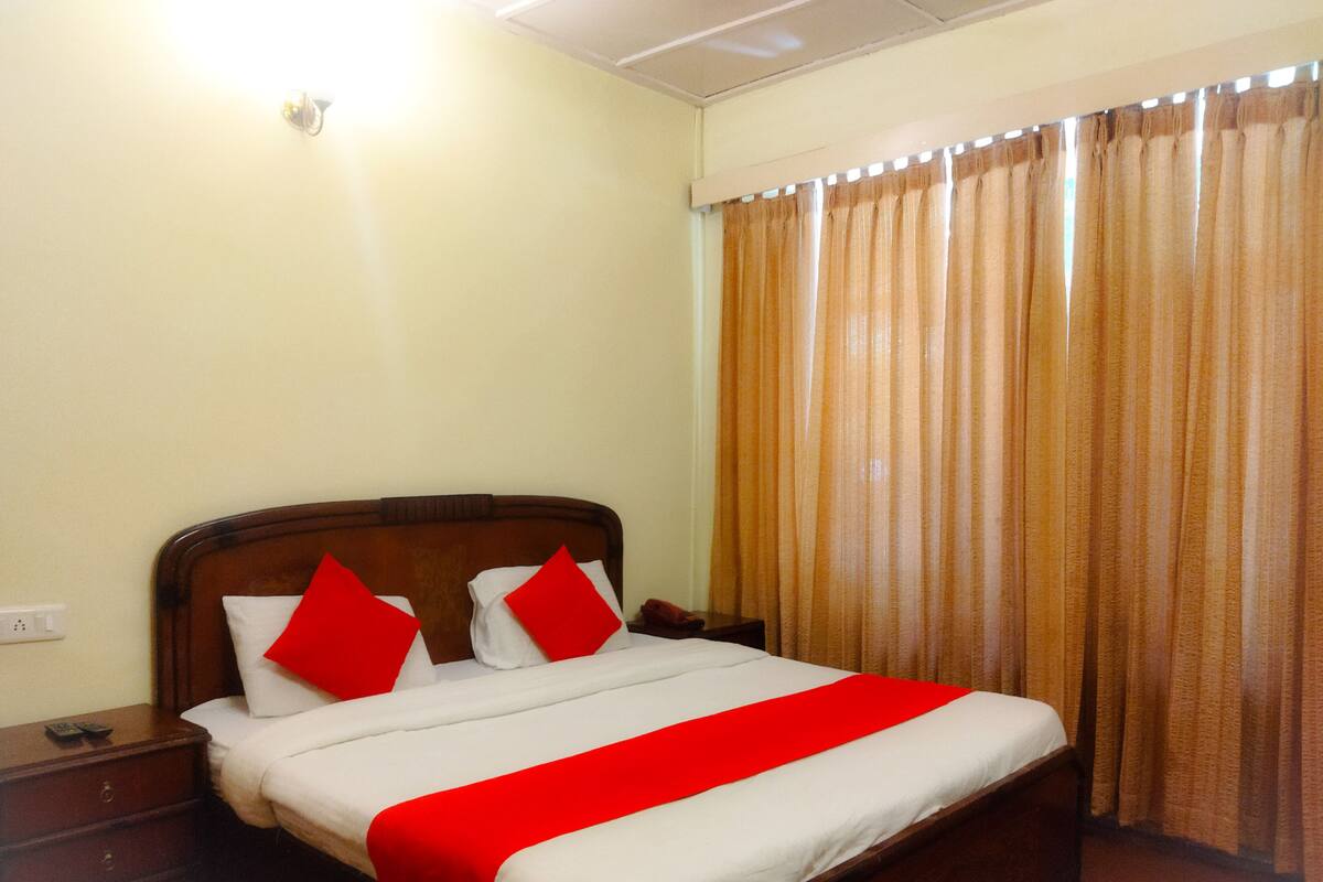 A hotel room with a wooden bed, red pillows, and a red bedspread.