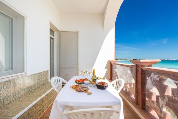 A balcony with a table set for dining, a bottle of wine, and a view of the sea.