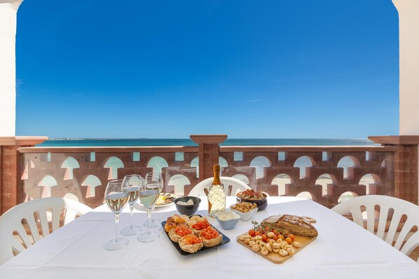 A table set with food and drinks, overlooking a clear blue sky and sea.