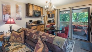 A cozy living room with a sofa, a dining table, a chandelier, and a view of a balcony with outdoor seating. - Apple Valley  52 at Rumbling Bald (Lake Lure)