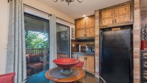 A kitchen with wooden cabinets, a black refrigerator, and a glass table with a red bowl. - Apple Valley  52 at Rumbling Bald (Lake Lure)
