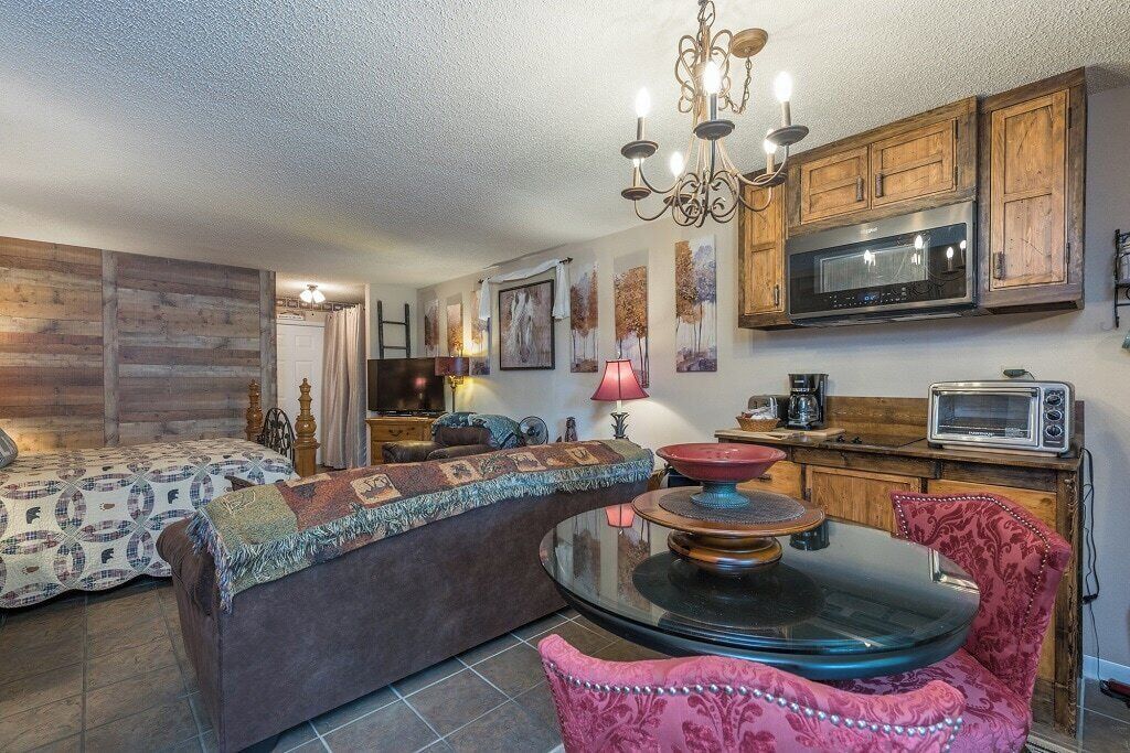 Ein gemütliches Zimmer mit einem Bett, einem Sofa, einem Esstisch mit Stühlen, einer Kandelaber, Holzschränken und einer Mikrowelle.