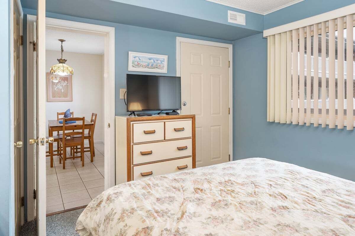 A bedroom with a bed, dresser, television, and a dining area with chairs and a table.