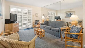 A living room with a grey sofa, wicker chairs, a television, and a large mirror. - 2 bedroom 2 bath with outdoor pool, oceanblock - great prices! (Ocean City)