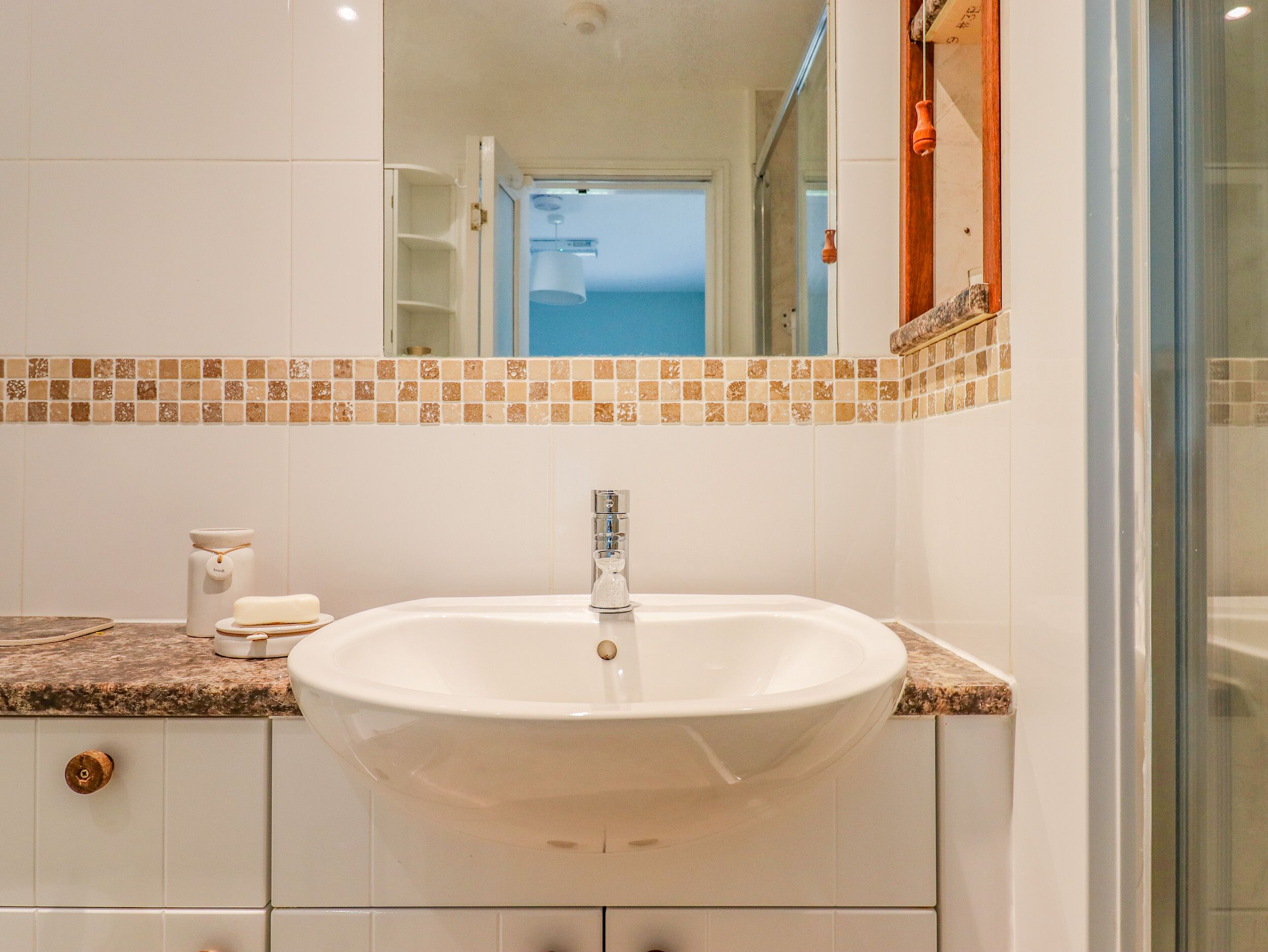 Een badkamer met een wit wastafelmeubel, een betegelde spatwand en een spiegel erboven.