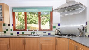 Eine Küche mit Holzausstattung, einer Edelstahl-Dunstabzugshaube, einem Fenster mit Blick auf Grünflächen und einer Fliesenrückwand.