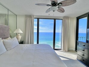 A hotel room with a large bed, a ceiling fan, a lamp, a dresser, and a view of the ocean. - Beautiful Beachfront Condo, Free Beach Ser., Pool, Great Balcony Views! (panama city beach)