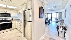 A modern kitchen with stainless steel appliances, white cabinetry, and a dining area with a view. - Beautiful Beachfront Condo, Free Beach Ser., Pool, Great Balcony Views! (panama city beach)