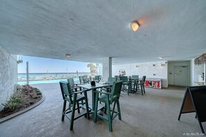 An outdoor seating area with tables and chairs, a pool in the background, and a view of the ocean. - Beautiful Beachfront Condo, Free Beach Ser., Pool, Great Balcony Views! (panama city beach)