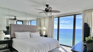 A hotel room with a large bed, a ceiling fan, a nightstand with a lamp, a dresser, and a view of the ocean. - Beautiful Beachfront Condo, Free Beach Ser., Pool, Great Balcony Views! (panama city beach)