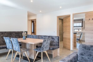 A modern dining area with a wooden table, cushioned seating, and a view into a kitchen. - Holiday Apartment "Aster Moments Apt Marie" with Mountain View, Balcony & Wi-Fi (San Genesio)