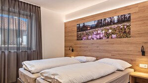 A double bed with white linens, a wooden headboard, a wall-mounted picture, and a bedside table with a lamp.