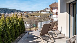 A balcony with two chairs, a view of a village, and a mountain in the background.