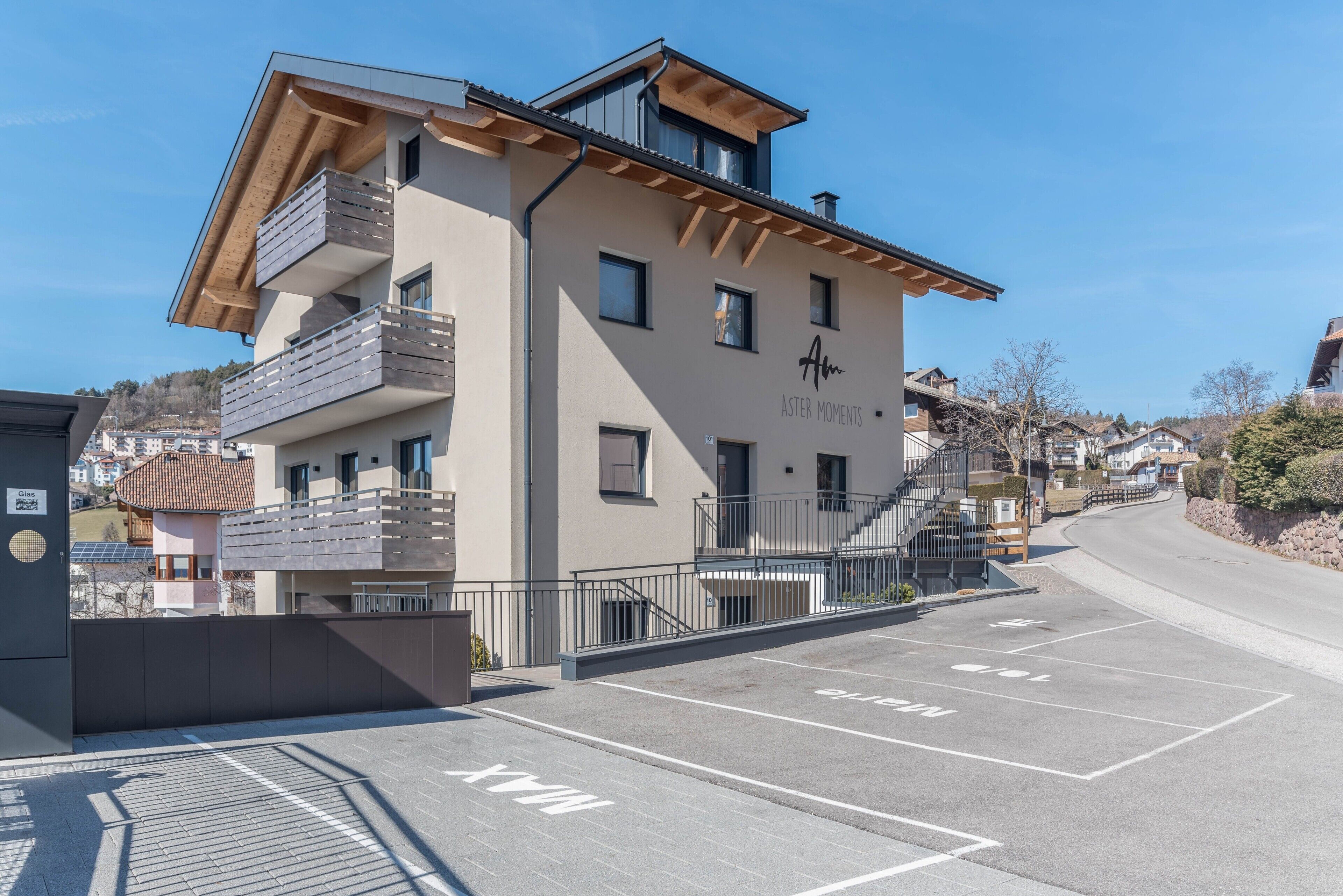 Un bâtiment moderne doté d’un balcon, d’un escalier et d’un espace de stationnement avec des places délimitées.