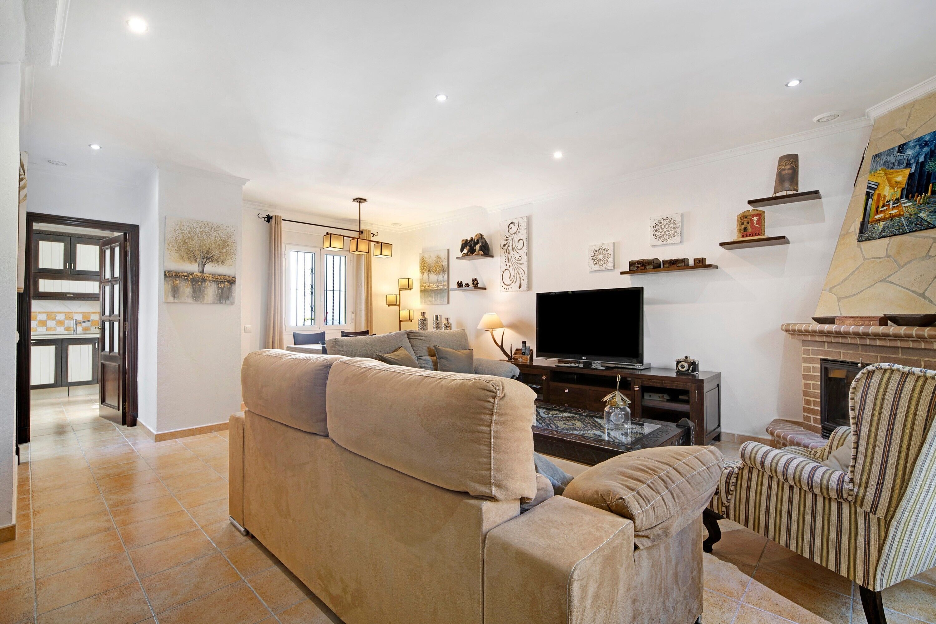 Een woonkamer met een bank, fauteuil, televisie, open haard en decoratieve wandkunst.